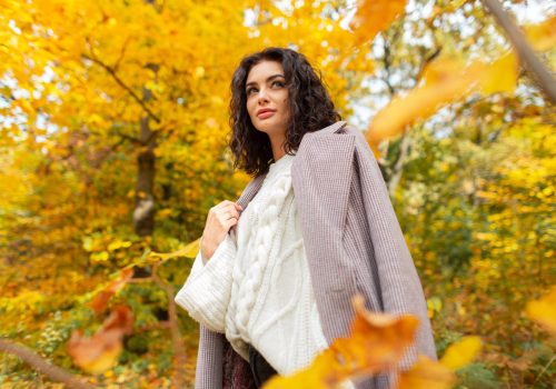 Beautiful curly autumn girl model in a fashionable coat with a knitted sweater walking in the autumn park with golden foliage