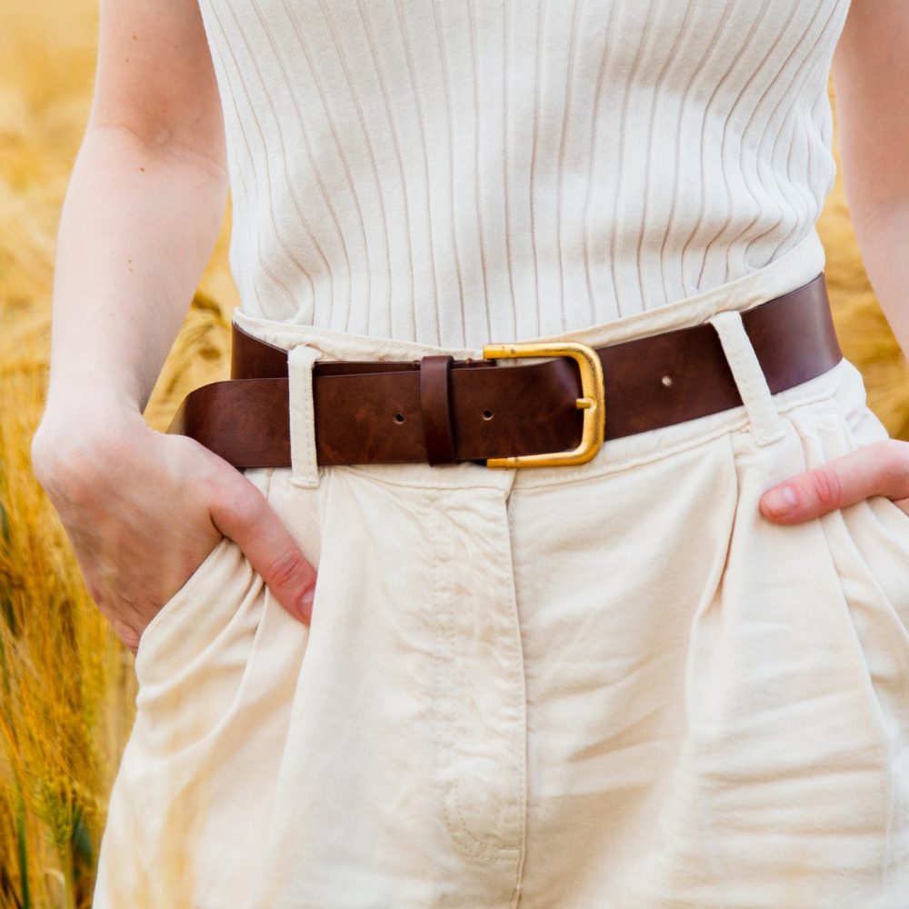 View on torso of woman in pants and belt with golden wheat on background